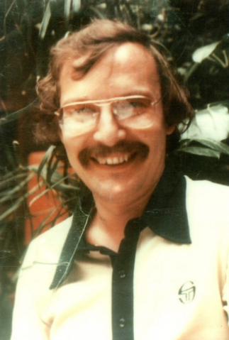 Headshot of man with glasses and mustache smiling outside