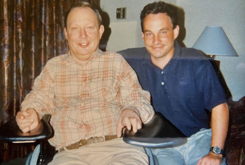Blue shirt young man sitting with an older man in wheelchair smiling