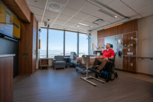 A bearded man in a power chair smiles as he enjoys his surroundings in an all-access, state-of-the-art hospital room at the Craig H. Neilsen Rehabilitation Hospital 
