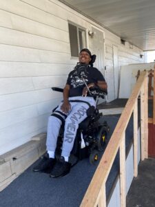 A man in a wheelchair smiles as he uses a modified ramp outside him home
