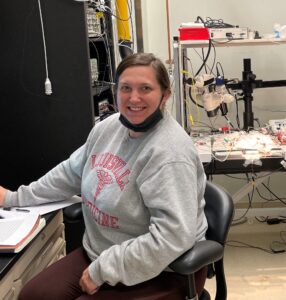 Smiling woman, wearing a gray sweater, at work in a scientific facility at Duke University