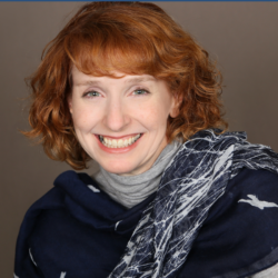 Smiling woman with short auburn hair wearing a navy blue scarf and gray turtleneck against a neutral background.