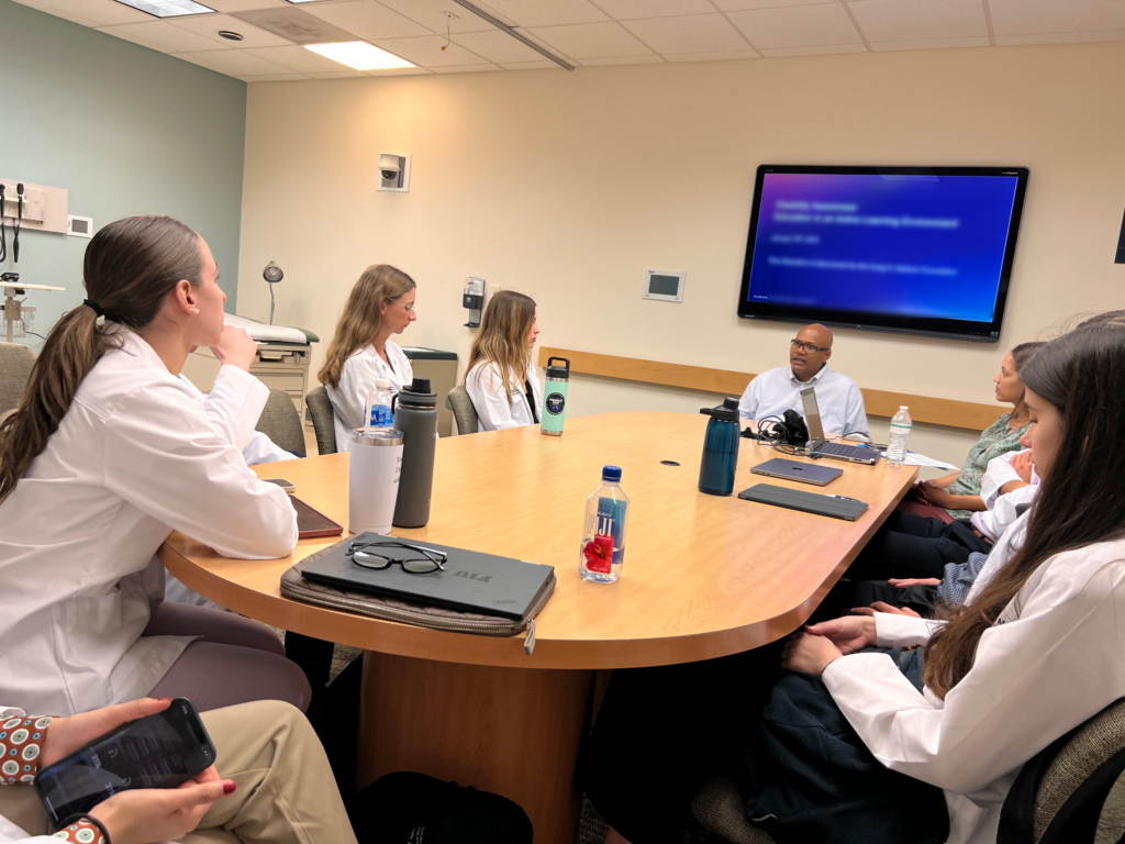 researchers in white coats sit around a desk during an information session